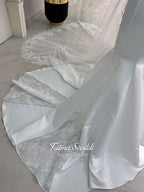 White mermaid satin-look hijab wedding dress with a high neckline, long sleeves, fitted bodice and floor-length train, styled with an intricate floral lace bridal veil. Fatma Sevildi Haute Couture modest bridal design.