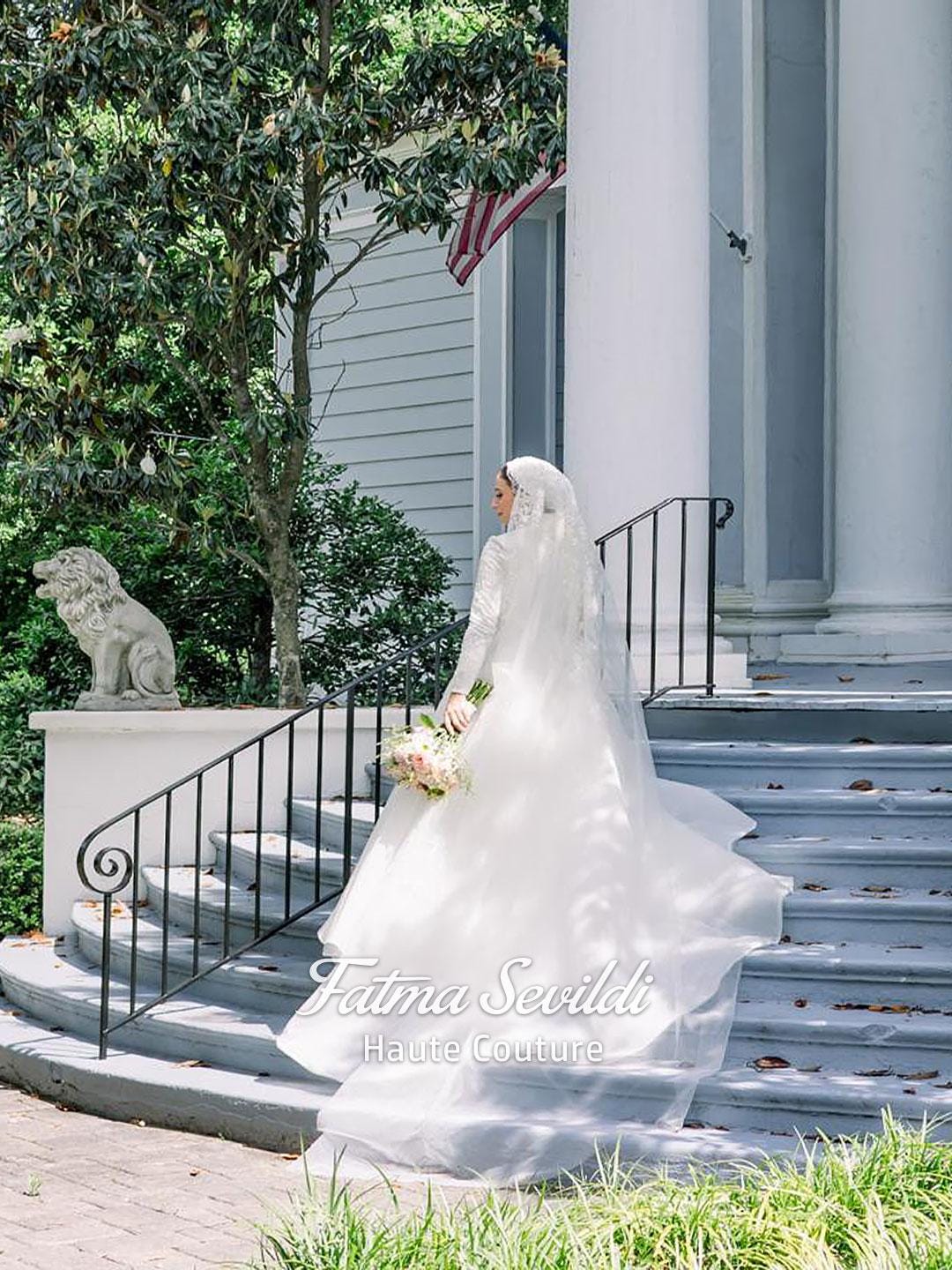 Elegant veiled hijab wedding dress with lace, beads, and long veil on bride descending steps