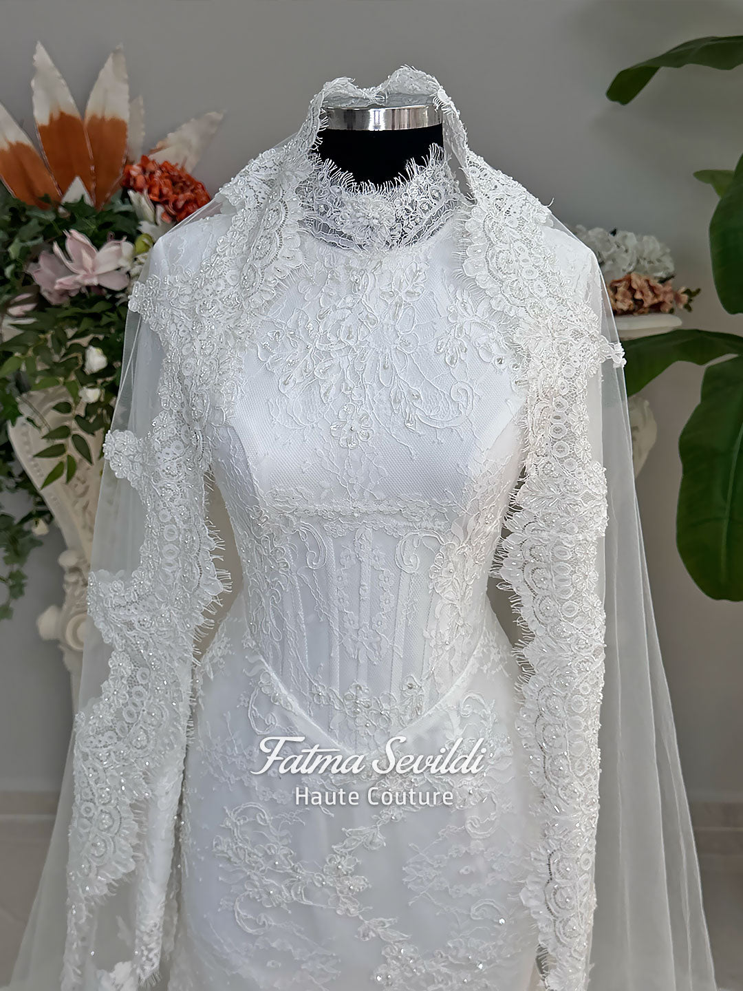 Luxury hijab wedding dress with mermaid silhouette and basque corset, featuring long sleeves, high neck lace, and a premium lace veil. Photographed on a mannequin in a bridal atelier setting.