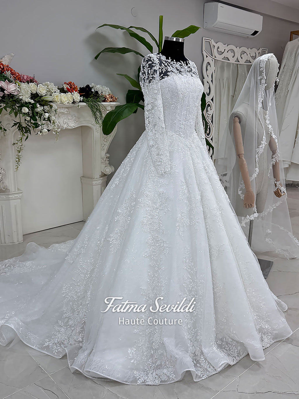 Luxury white hijab wedding dress with long floral lace sleeves, a beaded princess skirt, illusion boat neckline, and a matching premium lace-edged veil.