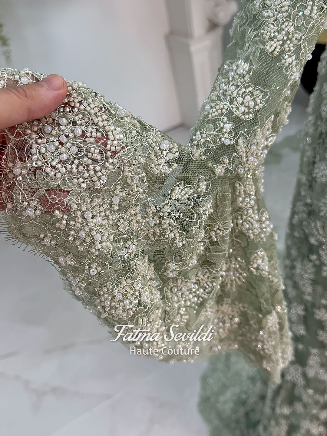 Sage green evening dress with beaded floral lace, a sweetheart neckline and long sleeves with flared lace cuffs, displayed on a mannequin.