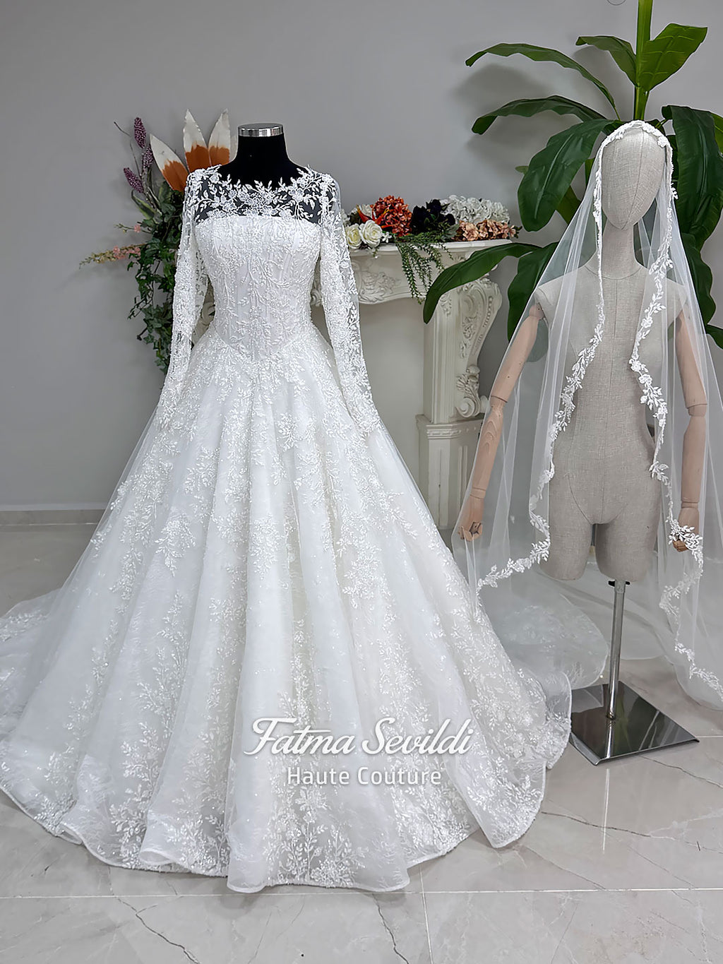Luxury white hijab wedding dress with long floral lace sleeves, a beaded princess skirt, illusion boat neckline, and a matching premium lace-edged veil.