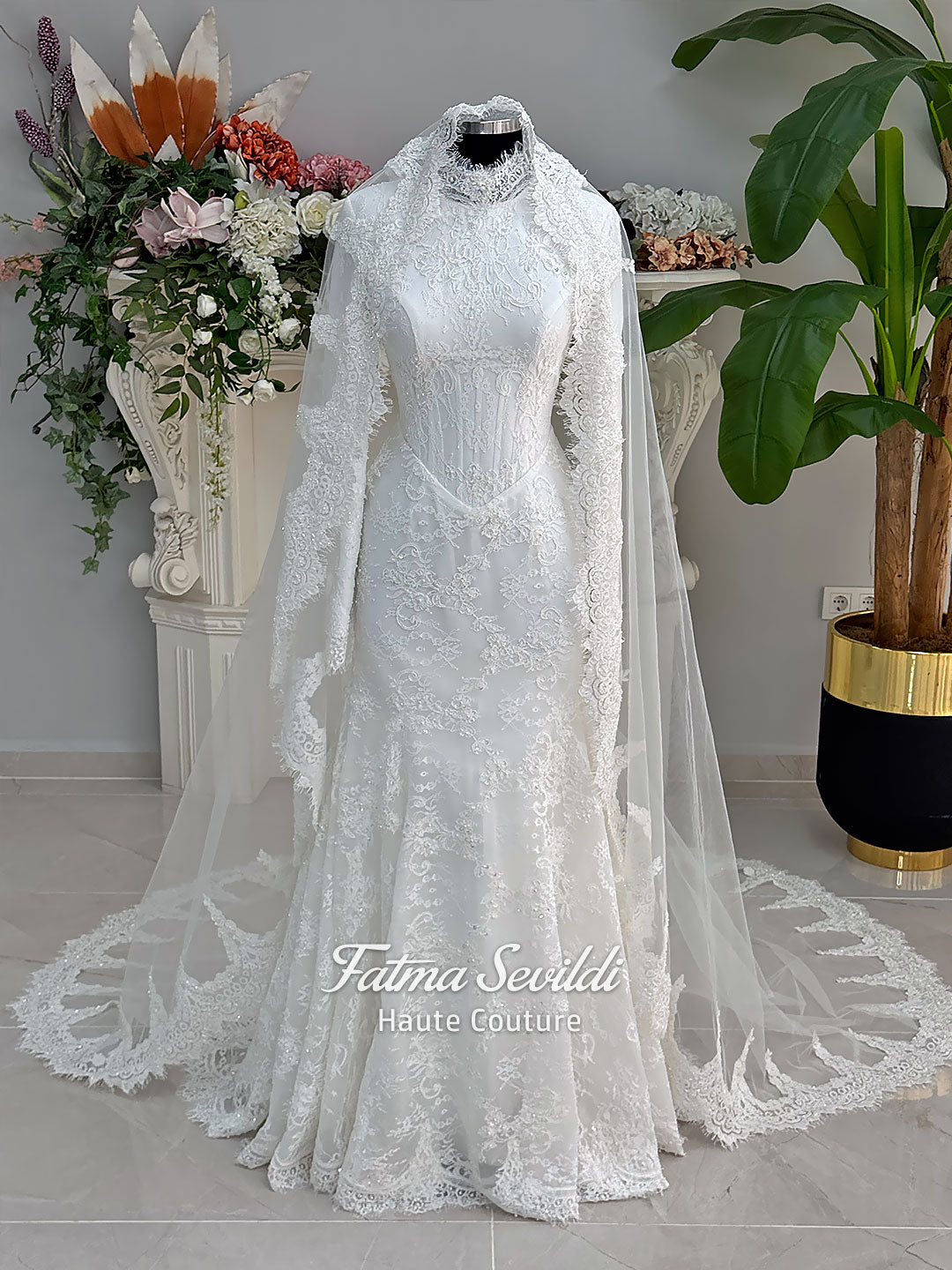 Luxury hijab wedding dress with mermaid silhouette and basque corset, featuring long sleeves, high neck lace, and a premium lace veil. Photographed on a mannequin in a bridal atelier setting.
