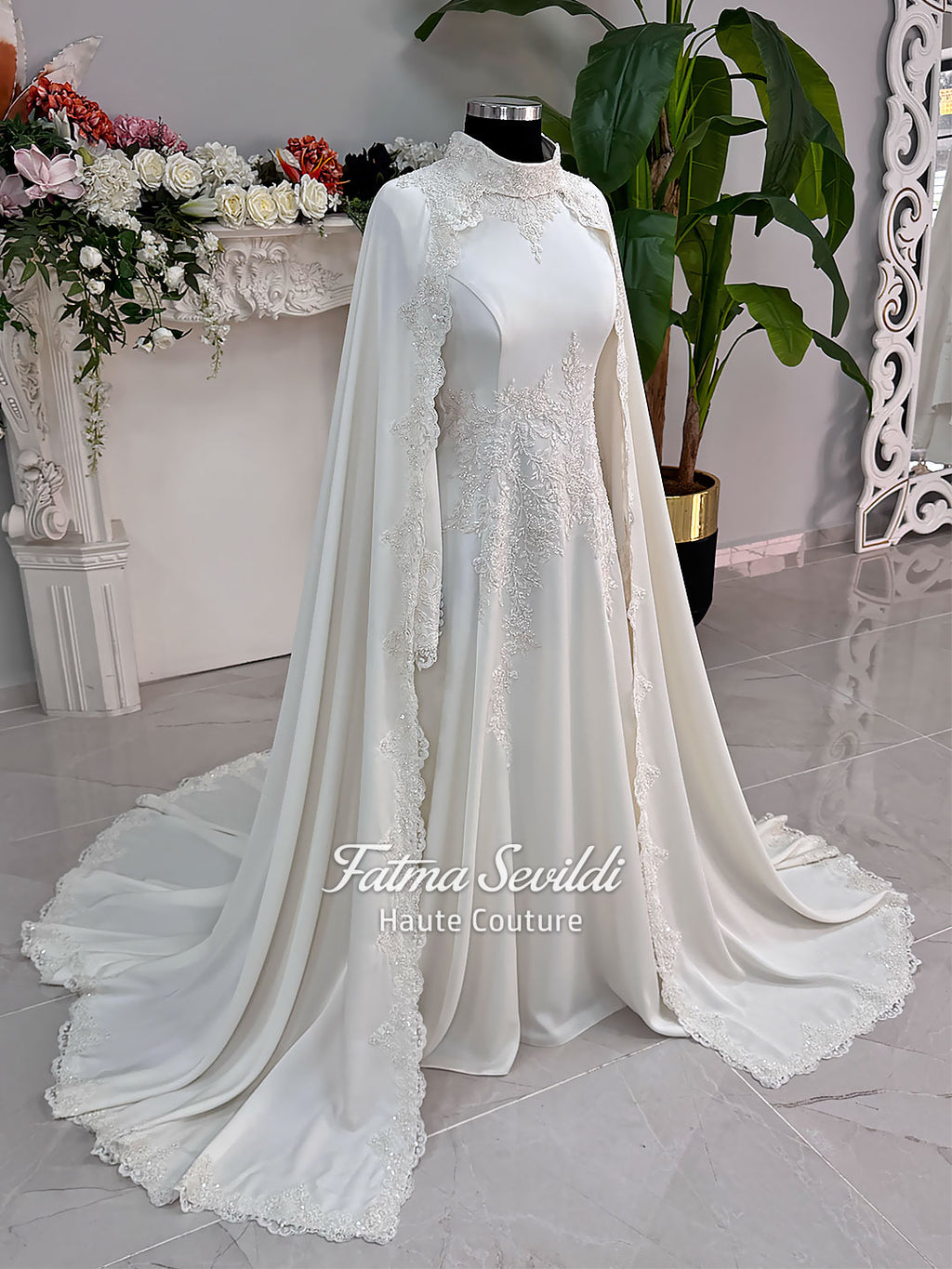 Ivory long sleeve hijab wedding dress with detachable lace-edged cape, floral beaded embroidery, high neckline and floor-length A-line modest bridal silhouette. Designed for Muslim brides seeking an elegant luxury wedding gown with full coverage.