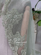 Sage green evening dress with beaded floral lace, a sweetheart neckline and long sleeves with flared lace cuffs, displayed on a mannequin.