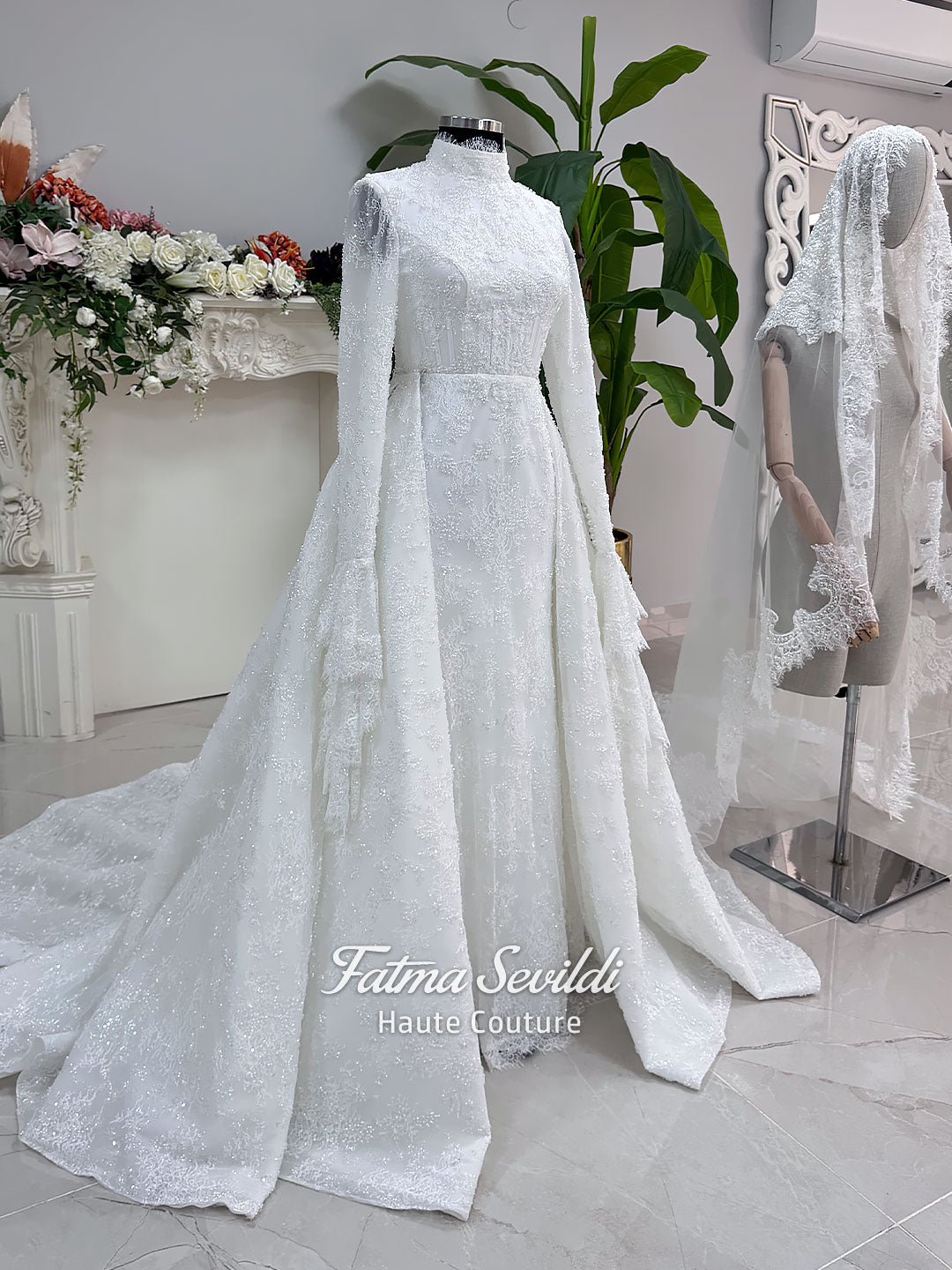 Luxury hijab wedding dress with long flounce sleeves, a high mock neckline, beaded floral lace, corset fit, mermaid silhouette, detachable overskirt, and included lace veil. Modest Muslim bridal gown shown from front, back, and detail views.