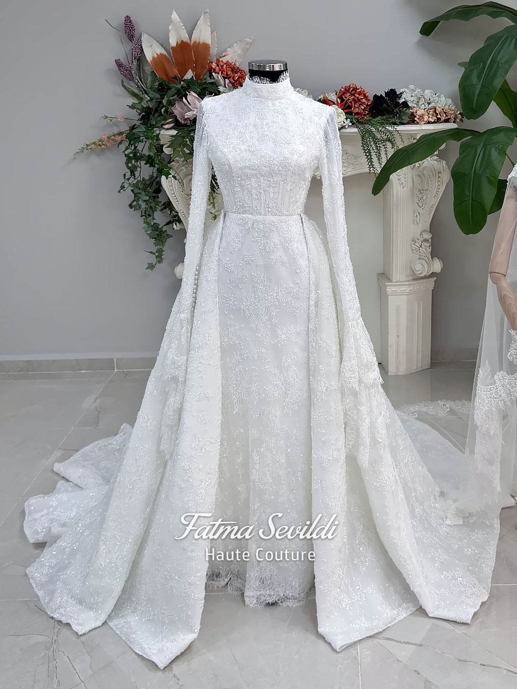 Luxury hijab wedding dress with long flounce sleeves, a high mock neckline, beaded floral lace, corset fit, mermaid silhouette, detachable overskirt, and included lace veil. Modest Muslim bridal gown shown from front, back, and detail views.