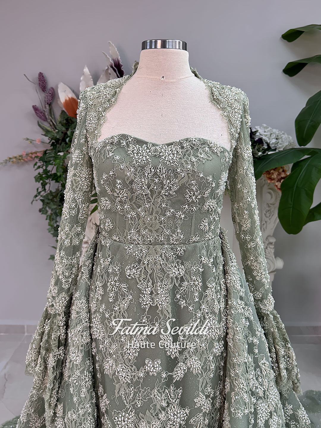 Sage green evening dress with beaded floral lace, a sweetheart neckline and long sleeves with flared lace cuffs, displayed on a mannequin.