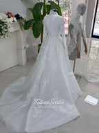 White hijab wedding dress with long sleeves, floral lace, high neckline and detachable overskirt, styled with a premium lace veil. Luxury modest bridal gown designed for a fully covered Muslim bridal look.