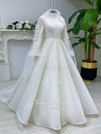 Luxury hijab wedding dress in an A-line tulle ball gown silhouette with long balloon sleeves, high neck, sparkling beadwork, and a lace-edged veil.
