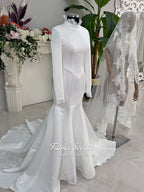 White mermaid satin-look hijab wedding dress with a high neckline, long sleeves, fitted bodice and floor-length train, styled with an intricate floral lace bridal veil. Fatma Sevildi Haute Couture modest bridal design.