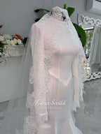 White mermaid satin-look hijab wedding dress with a high neckline, long sleeves, fitted bodice and floor-length train, styled with an intricate floral lace bridal veil. Fatma Sevildi Haute Couture modest bridal design.