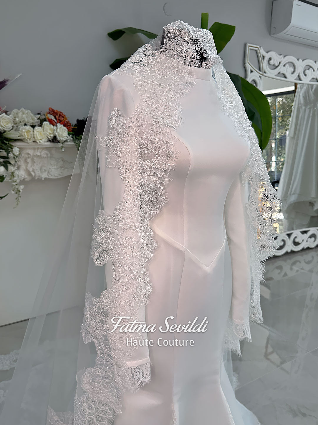 White mermaid satin-look hijab wedding dress with a high neckline, long sleeves, fitted bodice and floor-length train, styled with an intricate floral lace bridal veil. Fatma Sevildi Haute Couture modest bridal design.