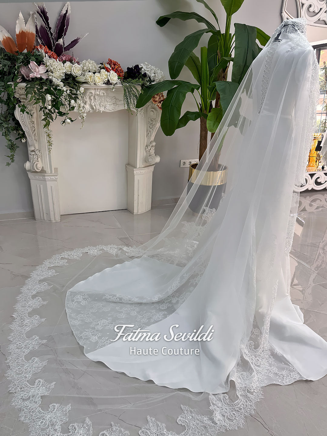 White mermaid satin-look hijab wedding dress with a high neckline, long sleeves, fitted bodice and floor-length train, styled with an intricate floral lace bridal veil. Fatma Sevildi Haute Couture modest bridal design.