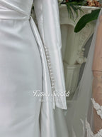 Luxury satin hijab wedding dress with off-shoulder long sleeves and an A-line silhouette, shown with premium lace veil and dramatic train. Custom couture modest bridal gown design with elegant draping and pearl details.