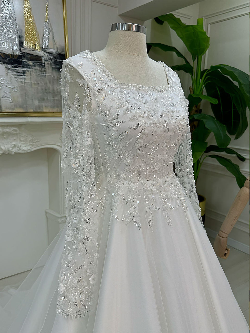 Elegant A-line lace wedding dress with square neck, long sleeves, beaded bodice, and veil on mannequin