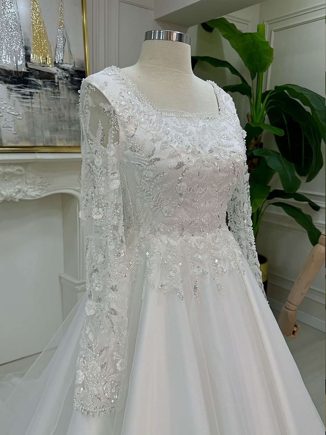 Elegant A-line lace wedding dress with square neck, long sleeves, beaded bodice, and veil on mannequin