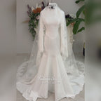 White mermaid satin-look hijab wedding dress with a high neckline, long sleeves, fitted bodice and floor-length train, styled with an intricate floral lace bridal veil. Fatma Sevildi Haute Couture modest bridal design.