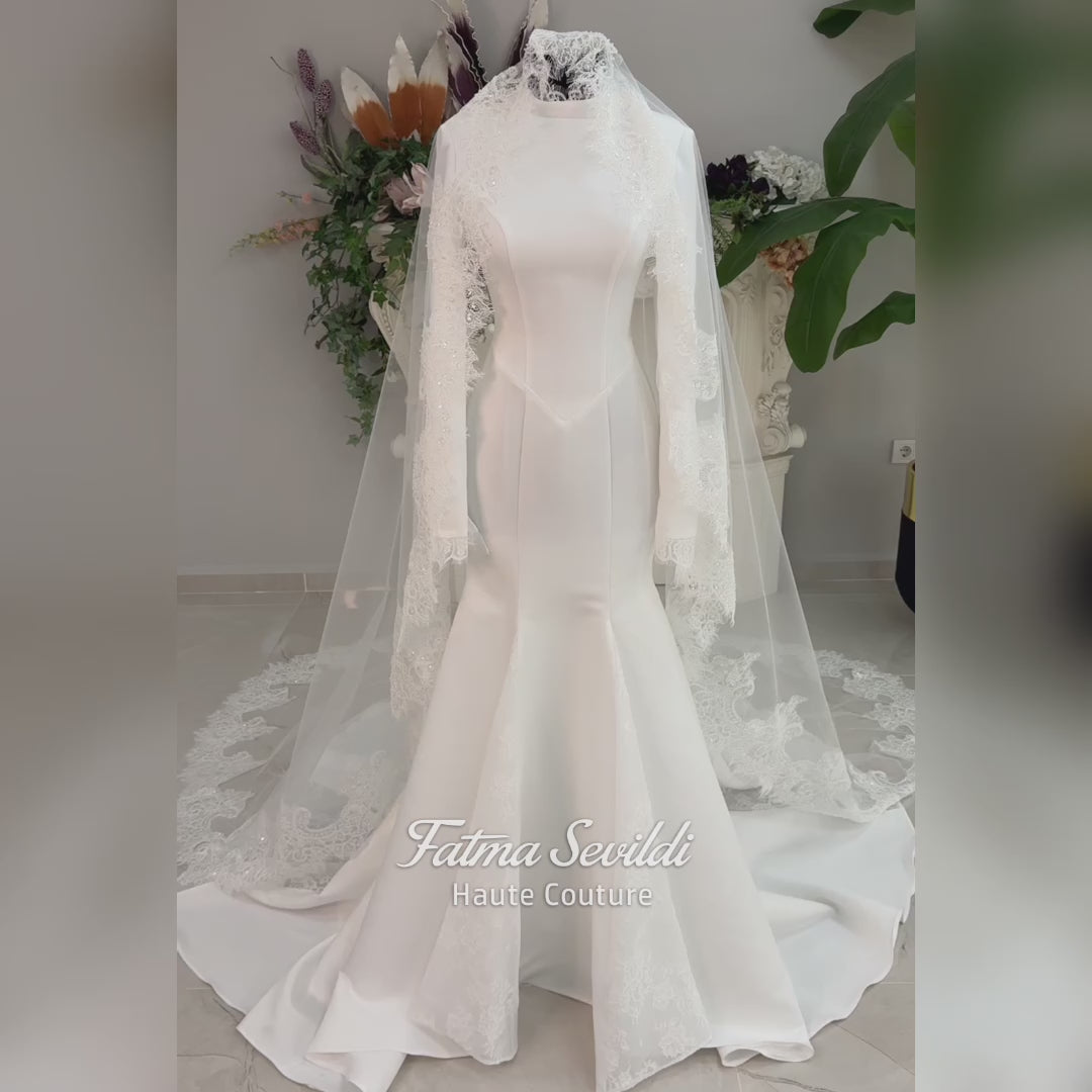 White mermaid satin-look hijab wedding dress with a high neckline, long sleeves, fitted bodice and floor-length train, styled with an intricate floral lace bridal veil. Fatma Sevildi Haute Couture modest bridal design.